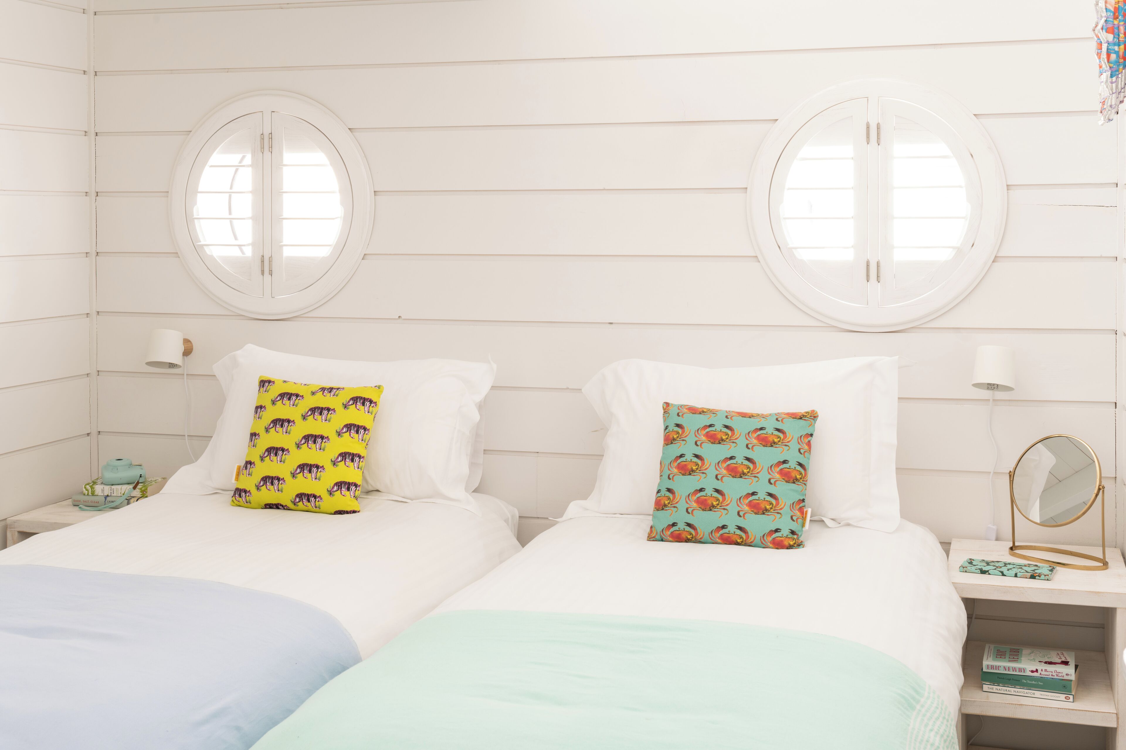 A room with two beds, each with a pillow and a bedside table with a lamp and a mirror.