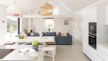 Eine moderne Küche mit weißen Schränken, ein Essbereich mit weißem Tisch und Bank sowie ein graues Sofa.