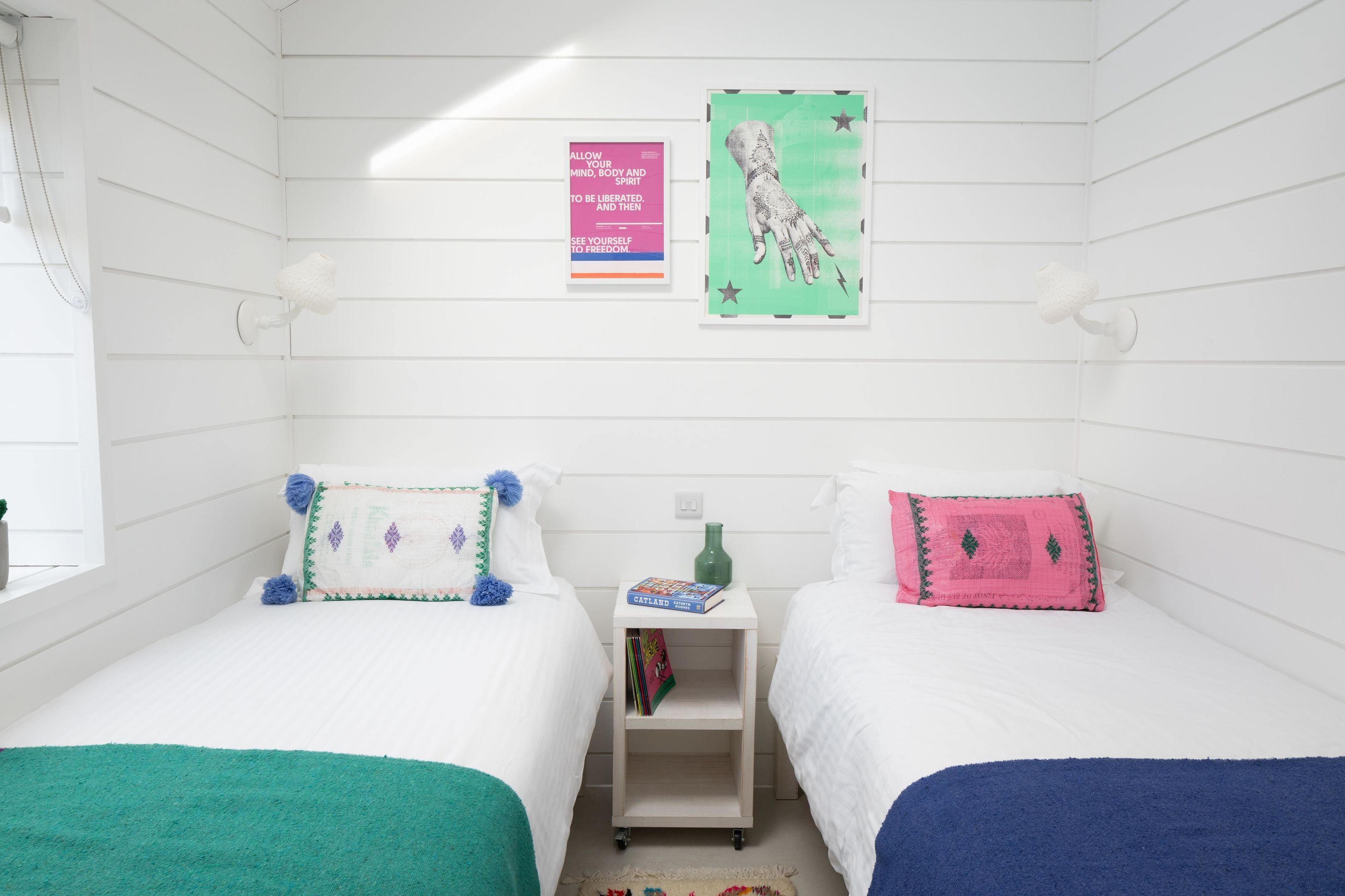 A room with two beds, a small shelf with books, and a wall with posters.