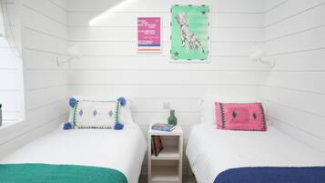A room with two beds, a small shelf with books, and a wall with posters.