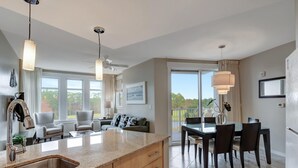 Une cuisine moderne dotée d’un grand îlot central, d’un coin repas avec des chaises foncées et d’une vue sur l’extérieur.