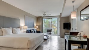 Une chambre d’hôtel moderne dotée d’un grand lit, d’un bureau, d’une chaise, d’une télévision et d’un balcon offrant une vue sur les arbres.
