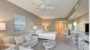 A modern hotel room with a bed, a sofa, a coffee table, a desk, and a TV.