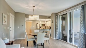 A modern dining area with a chandelier, a kitchen in the background, and a sliding glass door leading to an outdoor seating area.