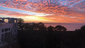 A sunset over a body of water with a view of a building and trees in the foreground.