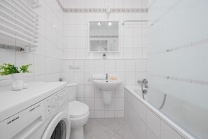 Een moderne badkamer met een Siemens wasmachine, toilet, wastafel en bad.
