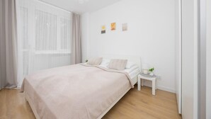 Un dormitorio moderno con cama, mesita de noche y ventana con cortinas translúcidas.