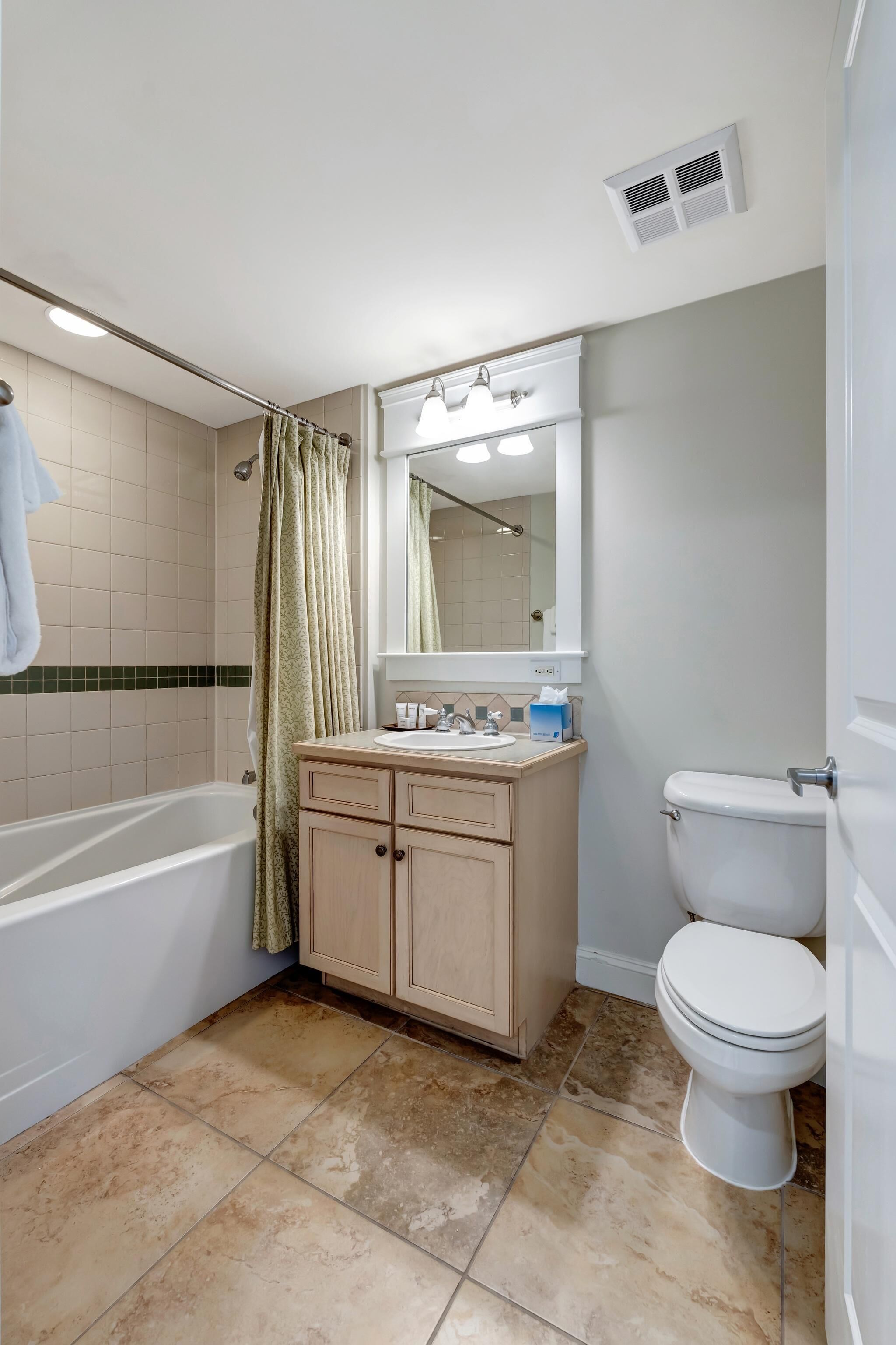 A bathroom with a bathtub, toilet, vanity with mirror, and a shower curtain.