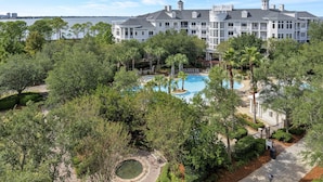 A large white building with multiple balconies and a pool area surrounded by trees. - Stunning Bay Views on the 6th Floor:  Two bedroom with Fully Equipped Kitchen, Sleeper Sofa at Sandestin Golf and Beach Resort! (Miramar Beach)