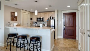 A modern kitchen with a central island, bar stools, stainless steel appliances, and a wooden door. - Stunning Bay Views on the 6th Floor:  Two bedroom with Fully Equipped Kitchen, Sleeper Sofa at Sandestin Golf and Beach Resort! (Miramar Beach)