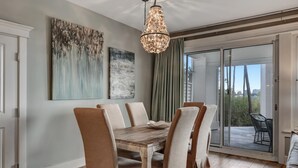 A dining area with a wooden table and cushioned chairs, a chandelier, and a sliding glass door leading to an outdoor patio.