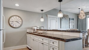 A modern kitchen with white cabinetry, a granite countertop, a built-in oven, and a large clock on the wall.