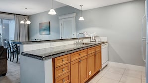A modern kitchen with granite countertops, wooden cabinets, a built-in dishwasher, and pendant lighting.