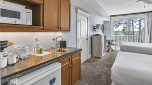 A hotel room with a kitchenette, a bed, a balcony with a table and chairs, and a view of the outdoors.