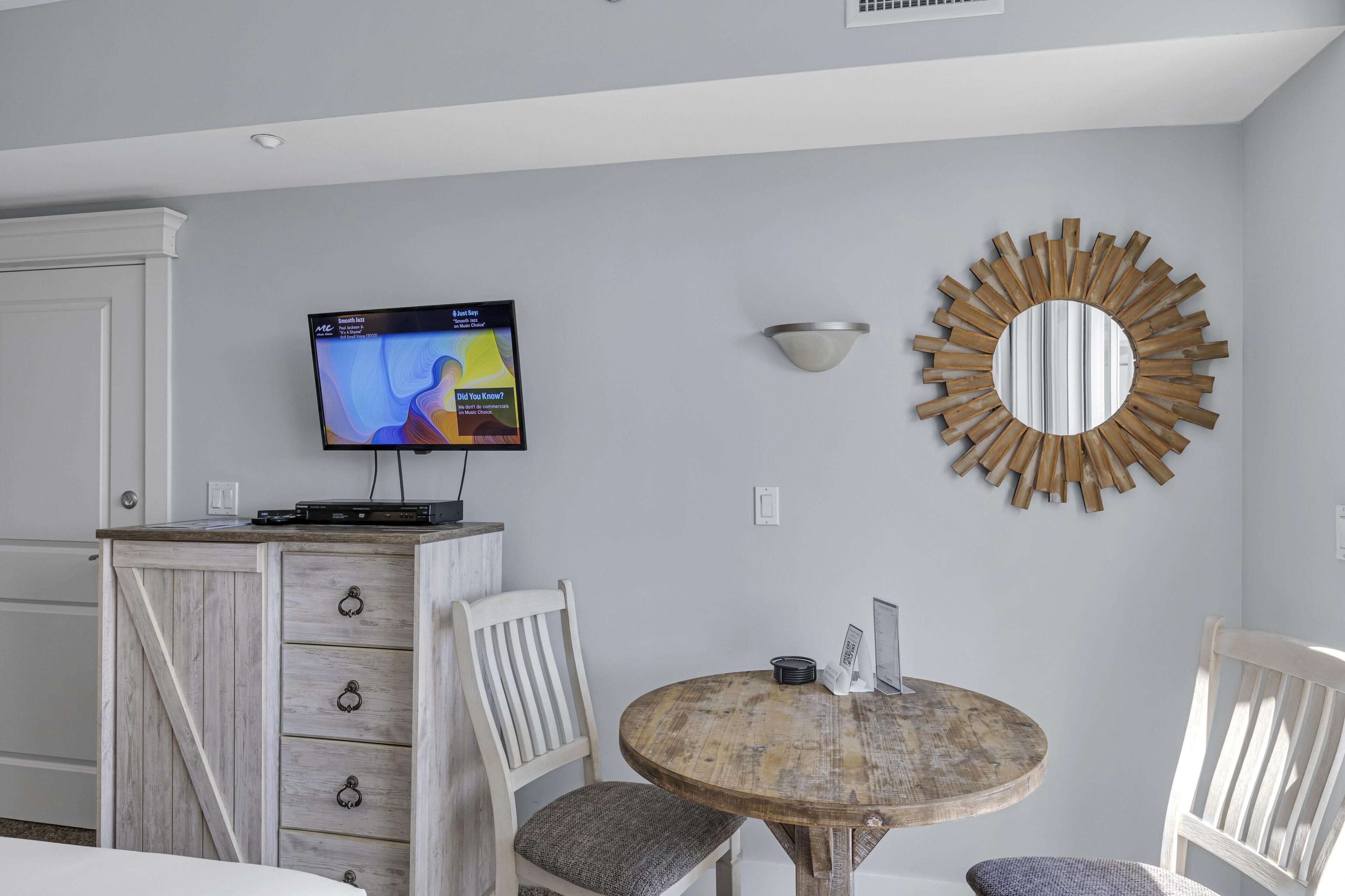 A modern living room with a television mounted on a cabinet, a round wooden table, and a decorative mirror on the wall.