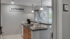 Cocina moderna con encimera de granito, pileta de acero inoxidable y muebles de madera. Incluye cafetera, tostadora y un reloj de pared decorativo.