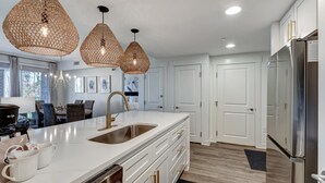 A modern kitchen with a large island, white cabinetry, stainless steel appliances, and woven pendant lights.