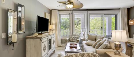 A living room with a television, a white cabinet, a sofa, a patterned armchair, and a ceiling fan.