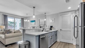 A modern kitchen with a central island, a dining area with a sofa, and a large window with curtains.