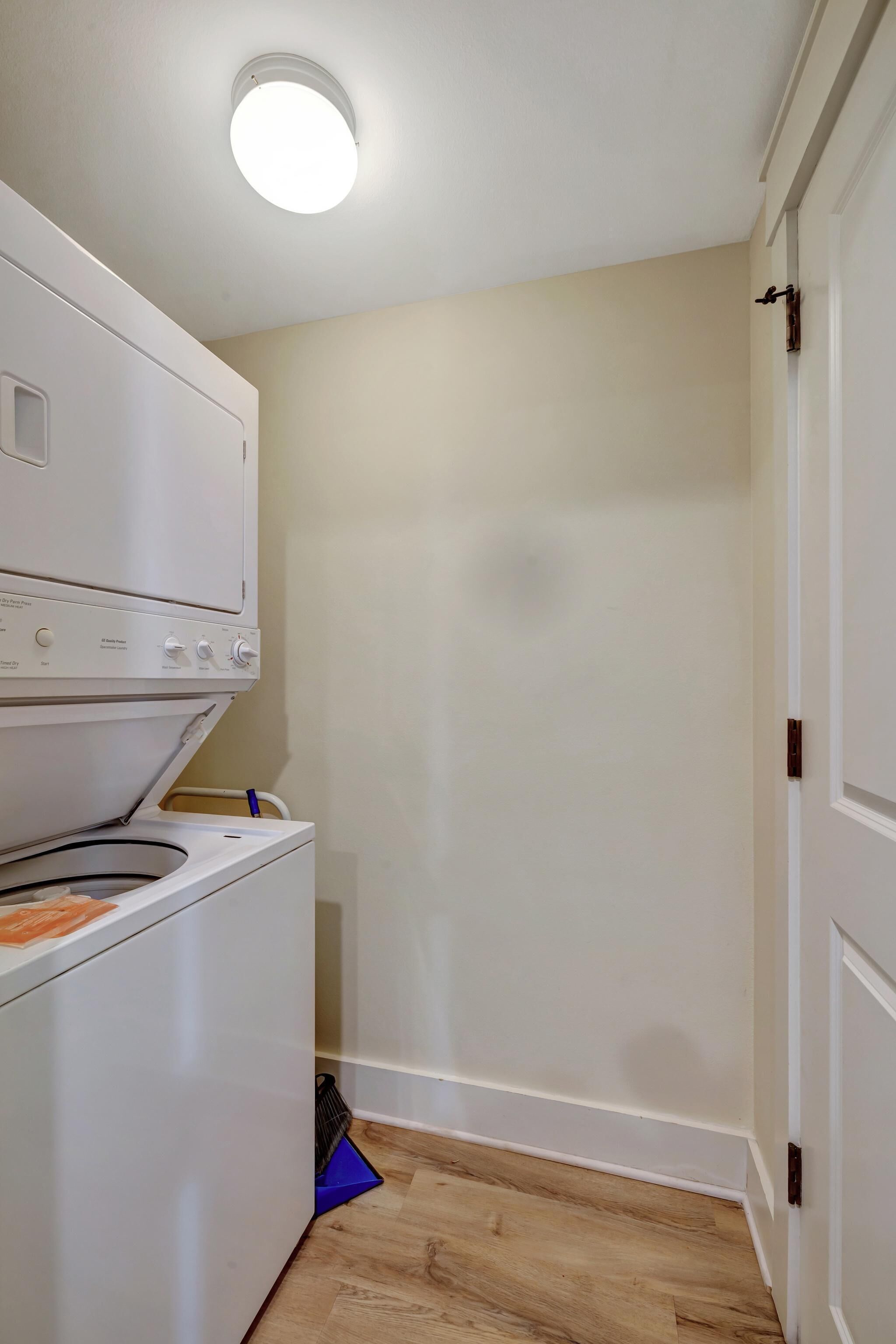 A laundry room with a stacked washer and dryer, a blue laundry basket, and a white door.