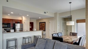 A modern kitchen with stainless steel appliances, a dining area with a marble table, and a gray sofa. - Relaxing Oasis in Luau: Serene Two-Bedroom Retreat with 3 Beds and Scenic Views at Sandestin Golf and Beach Resort! (Miramar Beach)