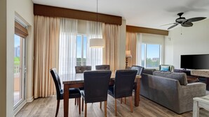 A modern living room with a dining area, large windows with curtains, a ceiling fan, and a flat-screen TV. - Relaxing Oasis in Luau: Serene Two-Bedroom Retreat with 3 Beds and Scenic Views at Sandestin Golf and Beach Resort! (Miramar Beach)