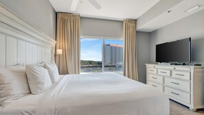 Habitación de hotel con una cama grande, un televisor de pantalla plana, un aparador y vistas a un paisaje urbano a través de un ventanal amplio.