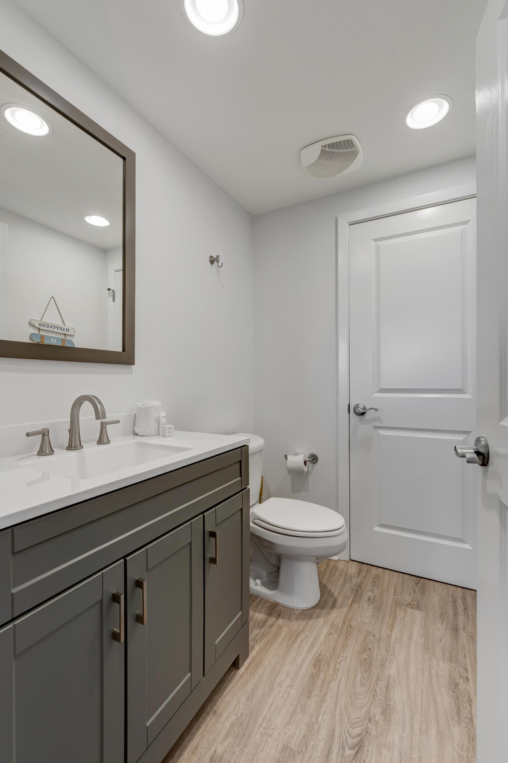 A bathroom with a white sink, a mirror, a toilet, and a door.