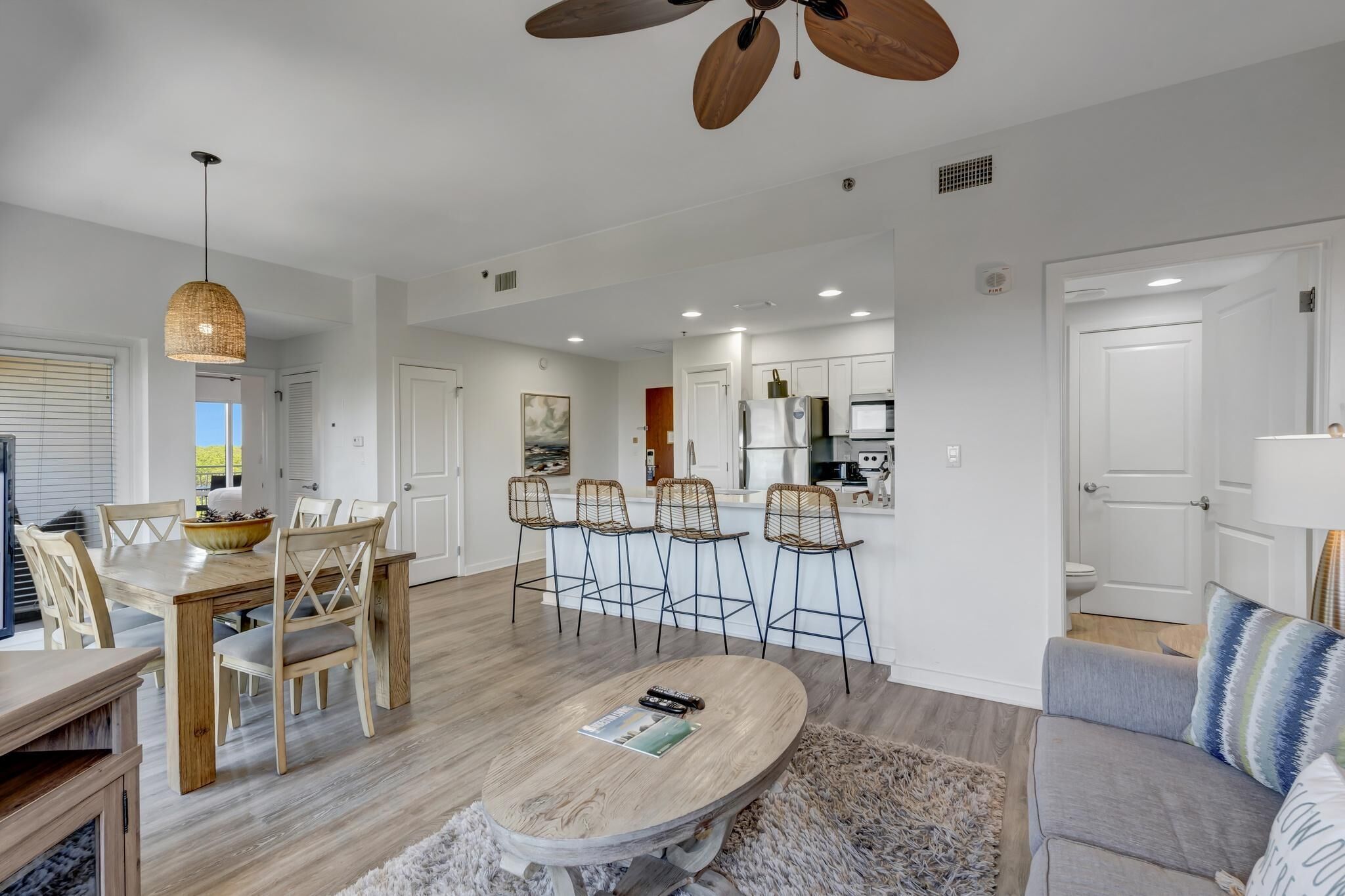 A modern living room with a dining area, a kitchen in the background, and a ceiling fan.