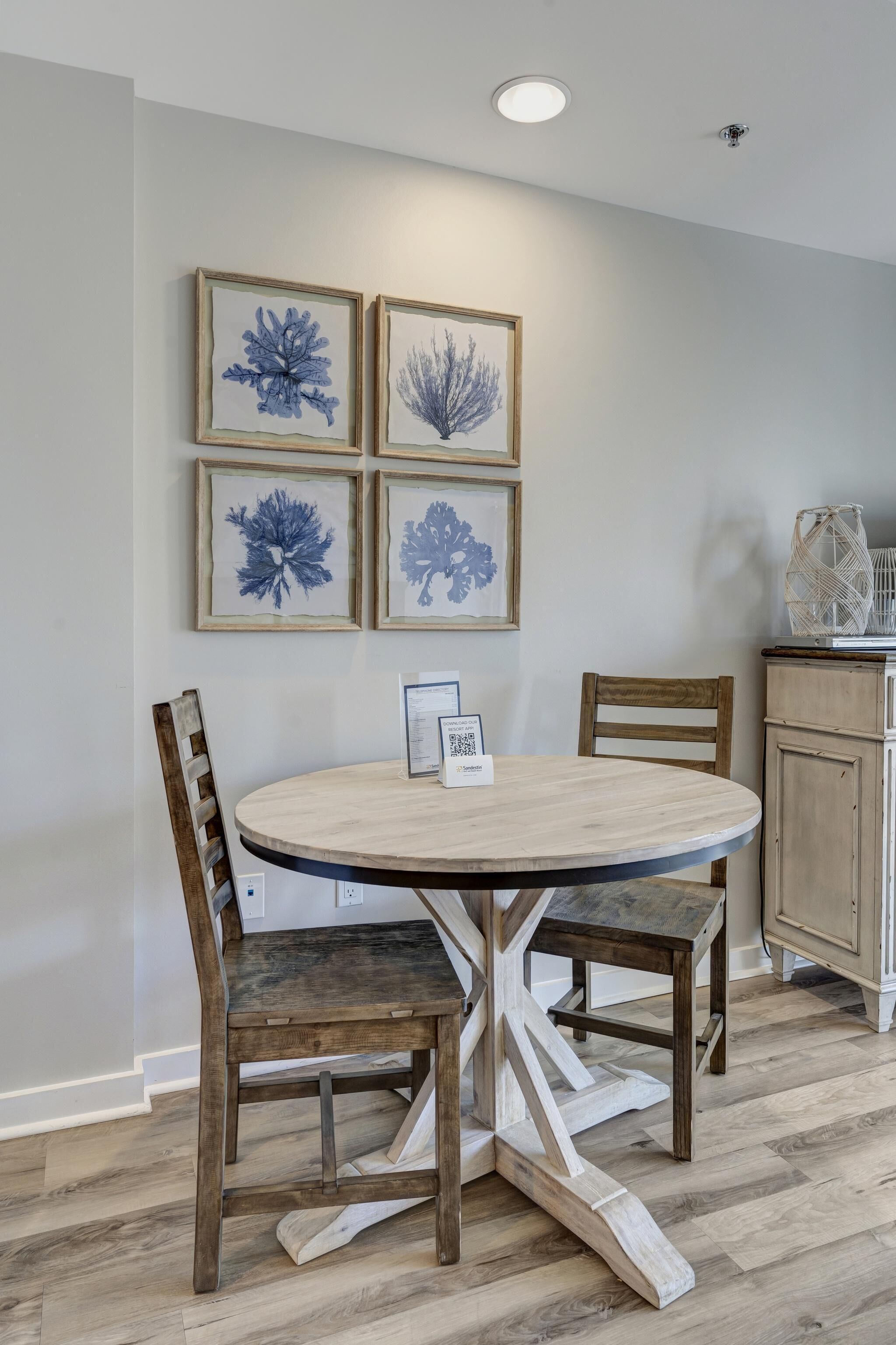 A dining area with a round table, four chairs, and framed artwork on the wall.
