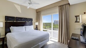 A hotel room with a large bed, a ceiling fan, a view of the city, and a desk with a TV.