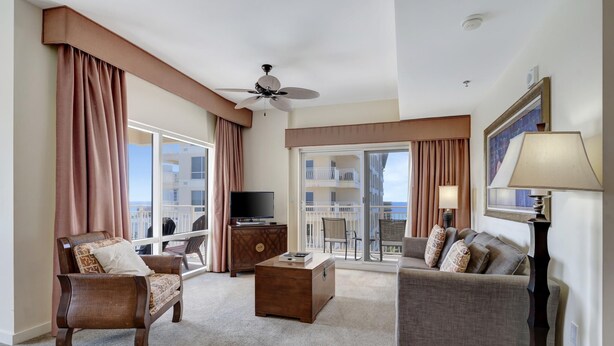 A hotel room with a balcony, a ceiling fan, a TV, a wooden chest, and a sofa.