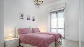 Un dormitorio con dos camas, una mesita de noche con lámpara, un candelabro y una ventana con cortinas.