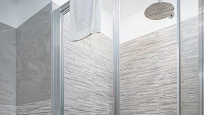 Un baño moderno con ducha de vidrio, azulejos de mármol gris y una toalla blanca colgada en la pared.