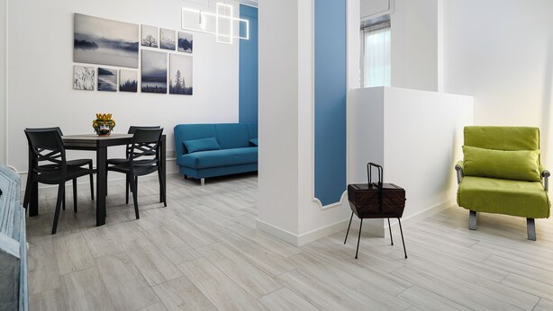 Una sala de estar moderna con comedor, un sofá azul, un sillón verde y una pared decorada con arte abstracto.