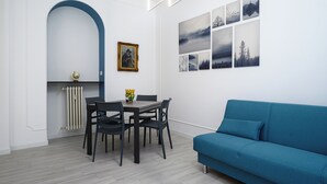 Una sala de estar moderna con un sofá azul, una mesa de comedor con sillas y una pared decorada con cuadros.