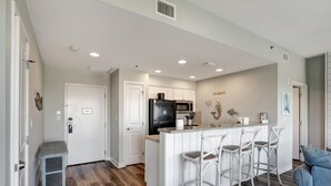 A modern kitchen with white cabinetry, a black refrigerator, and a bar area with white stools.