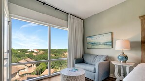 A room with a large window, a grey sofa, a round side table, and a lamp.