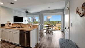 A modern kitchen with a large island, a dining area with a view, and a cityscape visible through the windows.