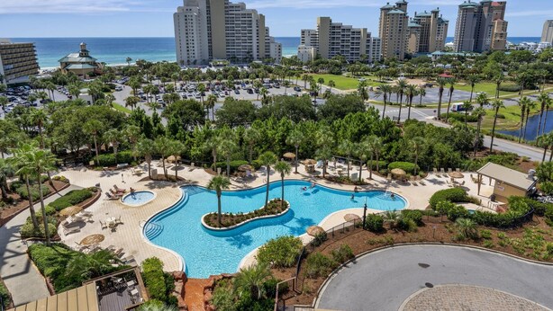 A resort with a large swimming pool, palm trees, and high-rise buildings in the background.