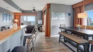 A modern hotel room with a kitchen area, dining table, and a large window with a city view.