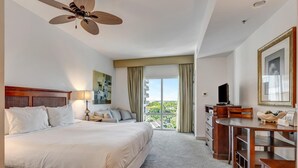 Habitación de hotel con una cama grande, un escritorio, una silla, un televisor y un balcón con vistas a la ciudad.