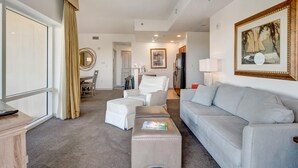 Un salón amplio con un sofá gris, un sillón blanco y una mesa de centro. Hay un ventilador de techo, un cuadro en la pared y un comedor al fondo.