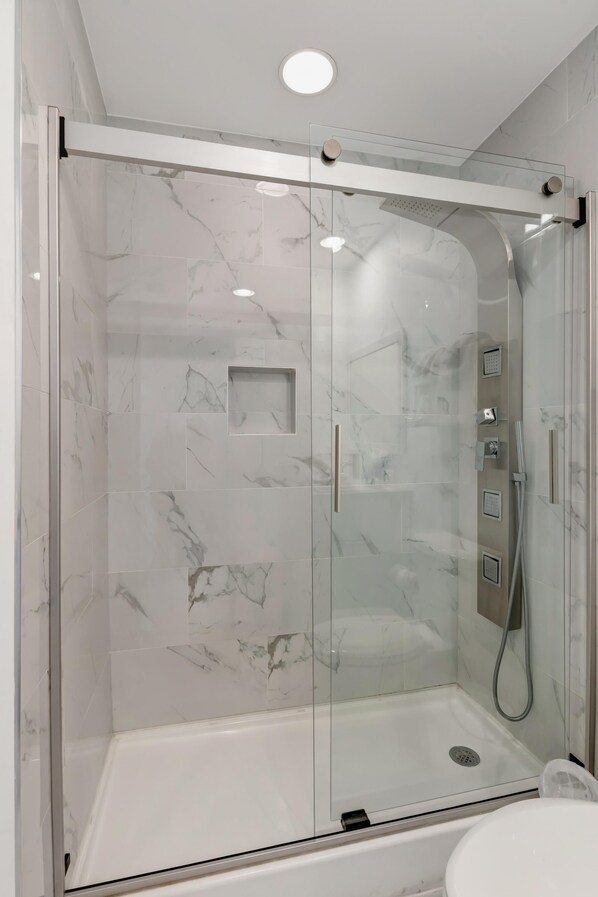 Una ducha con cerramiento de vidrio, pared con mosaicos de mármol, un cabezal de ducha manual y una manguera de ducha manual.
