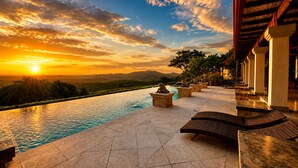 A poolside area with a view of the sunset over mountains, stone benches, and a covered walkway. - 5-Acre Private Jungle Estate | Ocean Views, Huge Pool, Chef & Transportation (Playa Tamarindo)