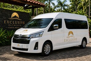 A white van with 'EXCLUSIVE RETREATS COSTA RICA' branding parked in front of a stone wall with greenery.