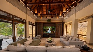 A spacious living area with a large sofa, a television, and a ceiling fan. - 5-Acre Private Jungle Estate | Ocean Views, Huge Pool, Chef & Transportation (Playa Tamarindo)