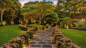 A stone pathway leading to a house surrounded by lush greenery and flowering plants. - 5-Acre Private Jungle Estate | Ocean Views, Huge Pool, Chef & Transportation (Playa Tamarindo)