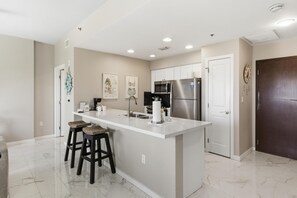 A modern kitchen with a white island, stainless steel appliances, and a dark wooden door.