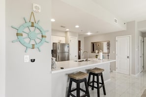 A kitchen with a white countertop, stainless steel appliances, and a decorative ship's wheel on the wall.